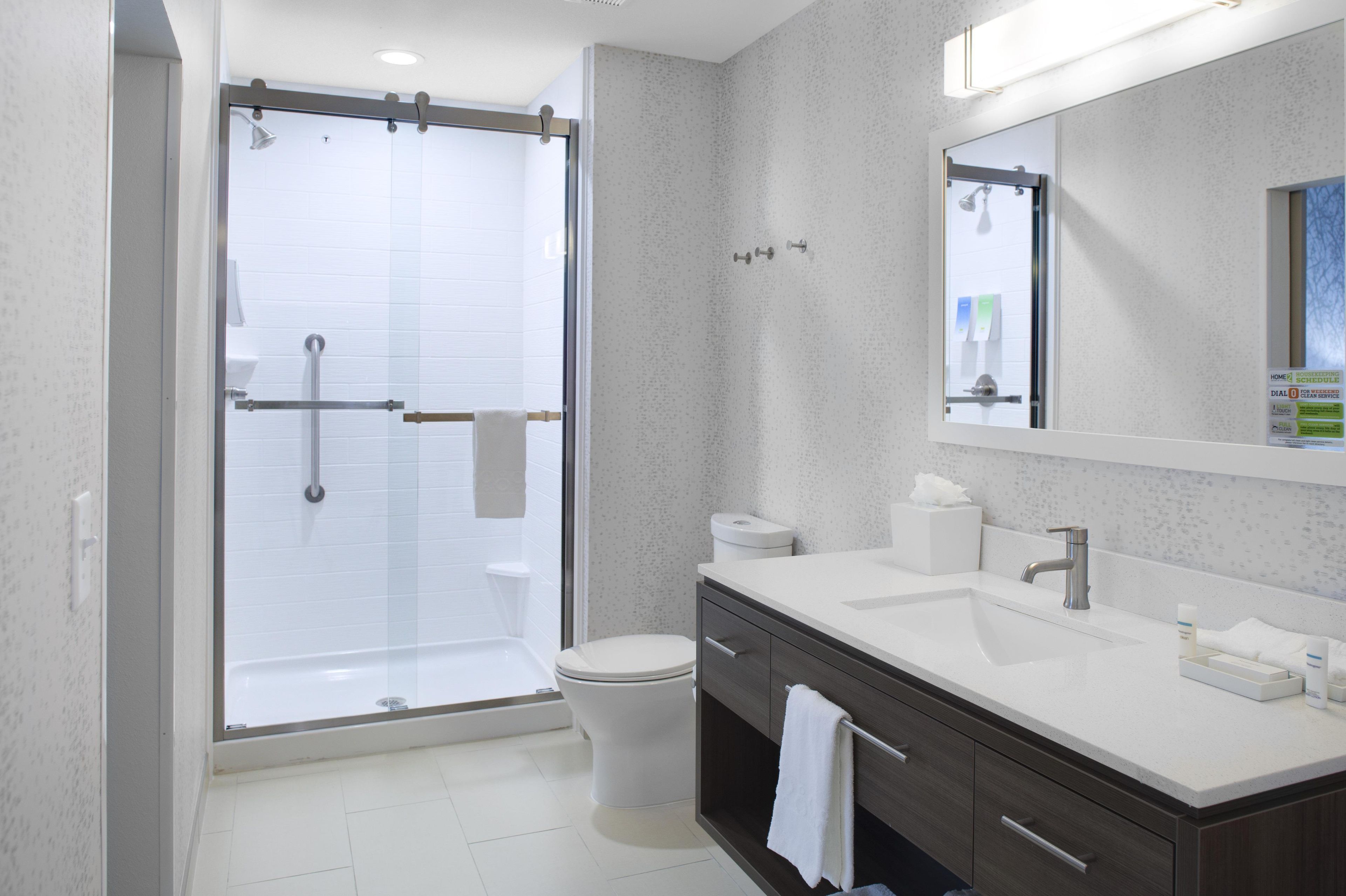 Un baño moderno con ducha, inodoro, tocador y un espejo grande.