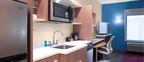 Una kitchenette compacta con refrigerador, microondas, lavaplatos y un pequeño comedor con una silla.