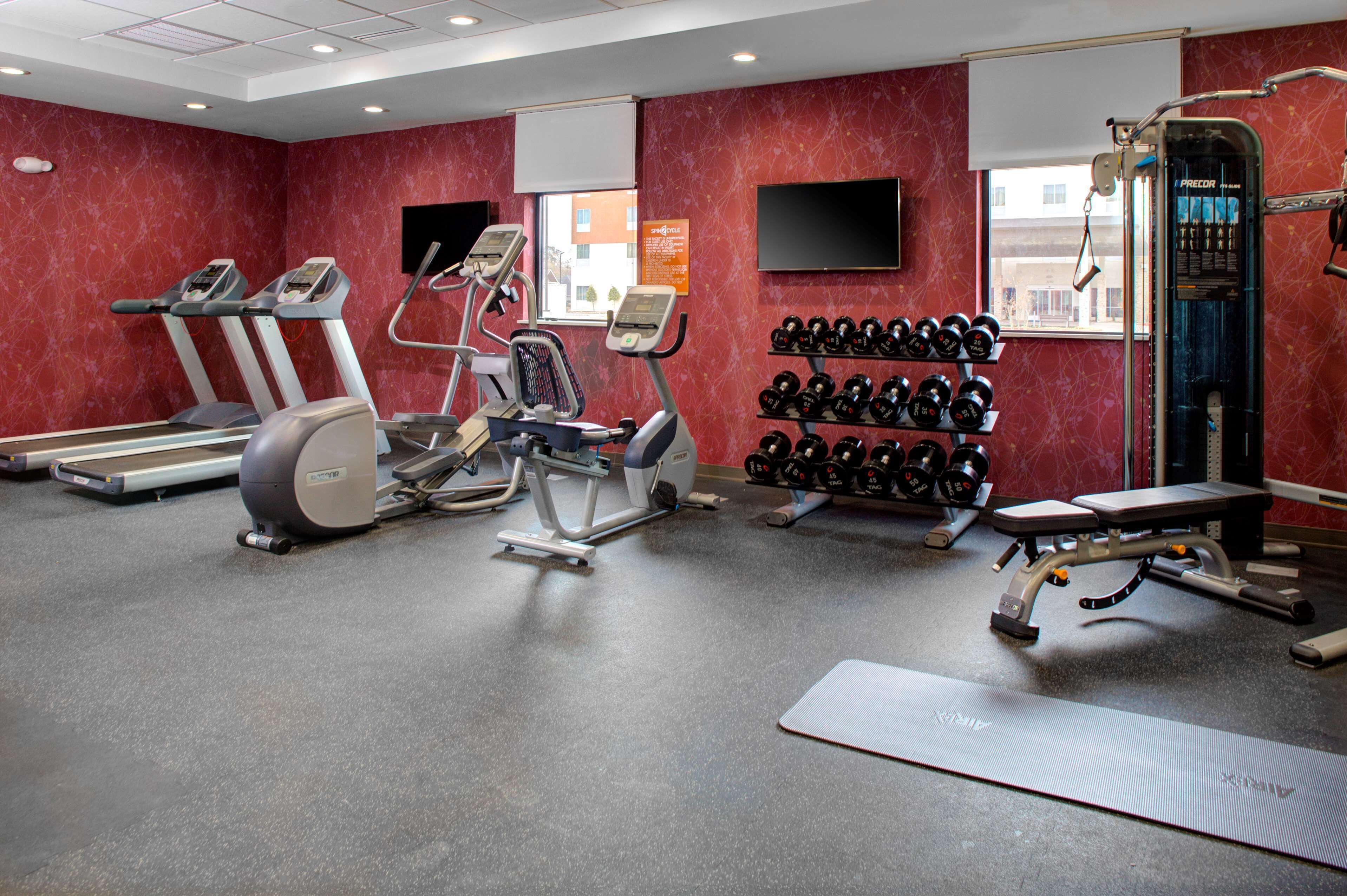A gym with treadmills, elliptical machines, a bench press, and a rack of dumbbells.