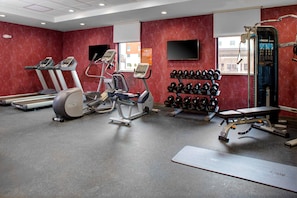 Un gimnasio con cintas de correr, elípticas, una prensa de banca y una barra con mancuernas.