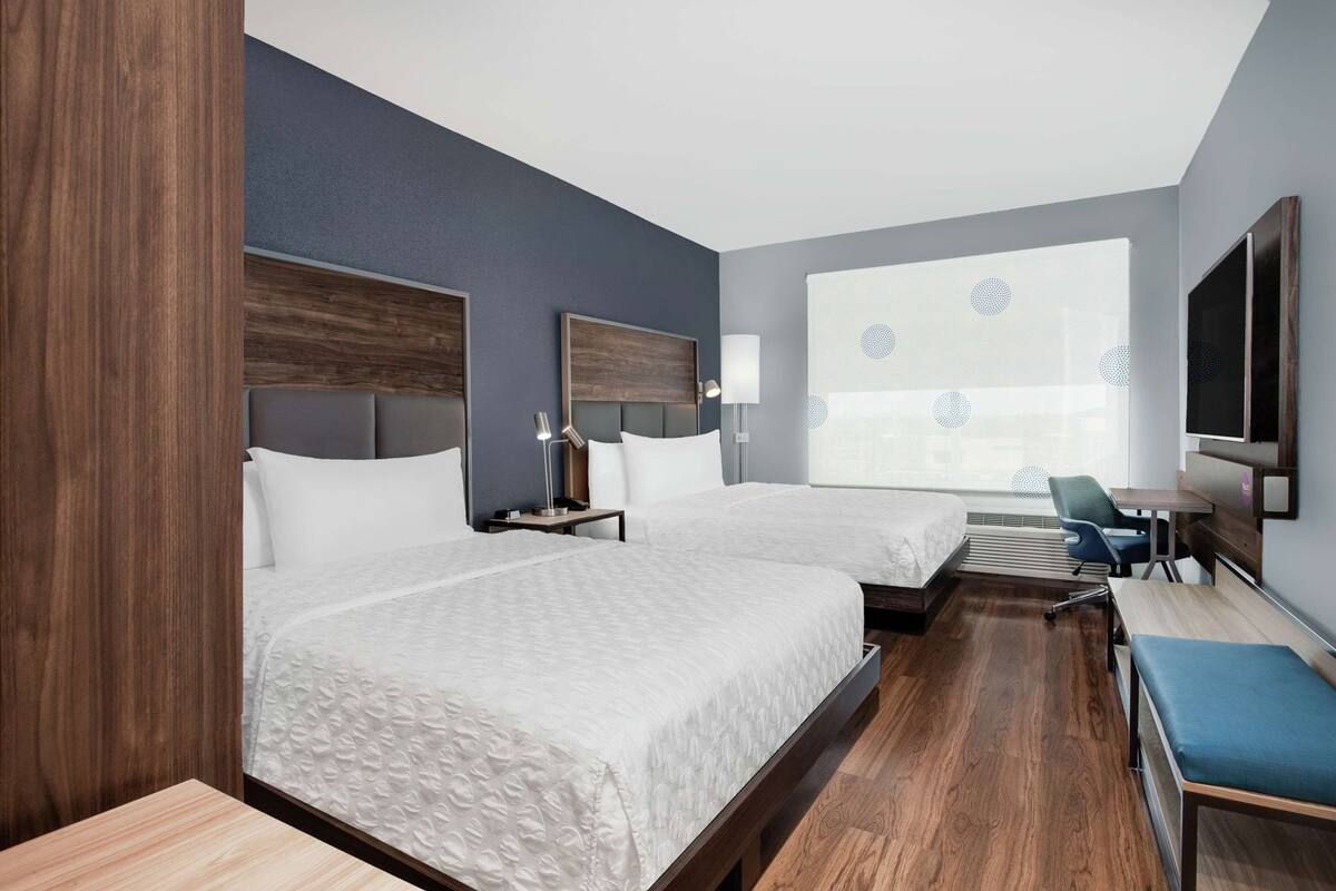 Une chambre d’hôtel avec deux lits, un bureau, une chaise, une télévision et une grande fenêtre donnant sur un beau paysage.