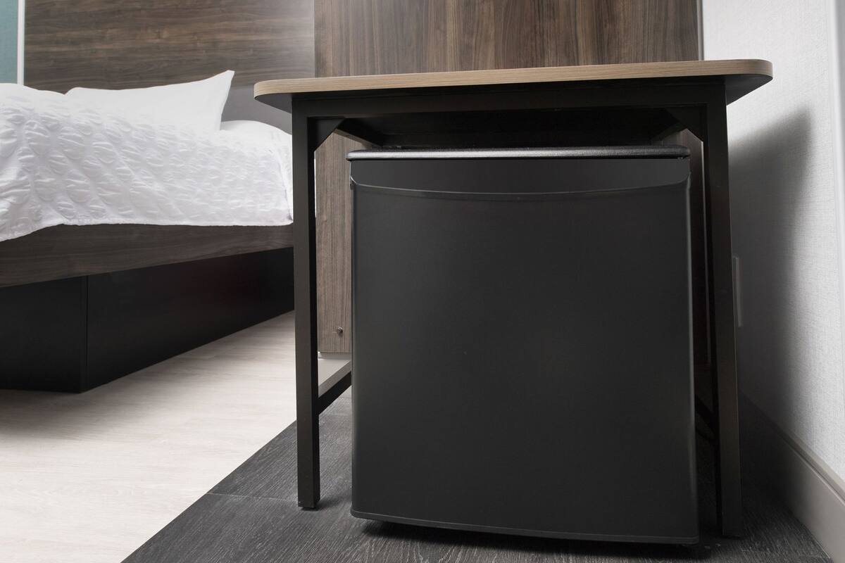 Une petite table d’appoint au design épuré, dotée d’un cadre noir et d’un plateau en bois, placée à côté d’un lit dans une chambre à coucher moderne.
