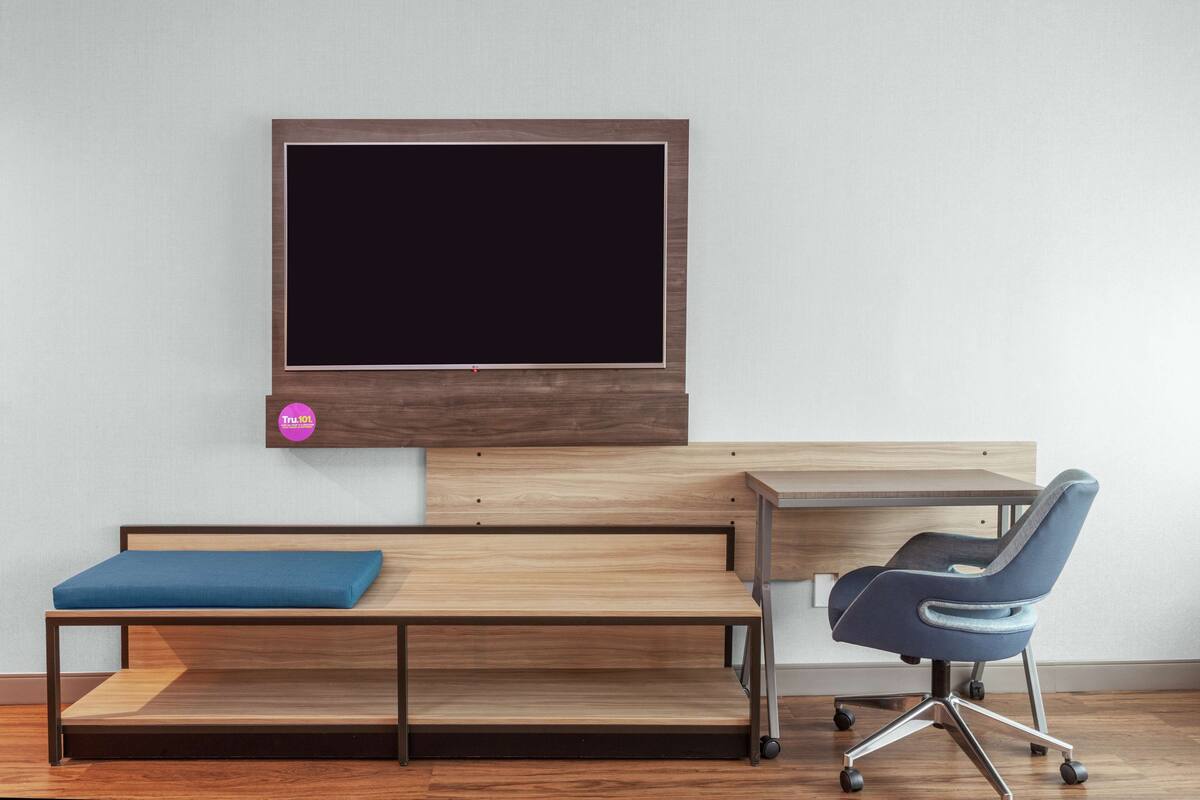 Une chambre moderne avec un bureau en bois, un banc bleu rembourré, un téléviseur fixé au mur et une chaise de bureau bleue.
