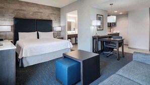 Une chambre d’hôtel avec un lit, un bureau, une chaise et un petit pouf bleu.