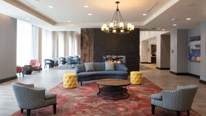 Un hall d’entrée spacieux, agrémenté d’un lustre moderne, d’un canapé bleu, de fauteuils à motifs et d’un tapis rouge à motifs.