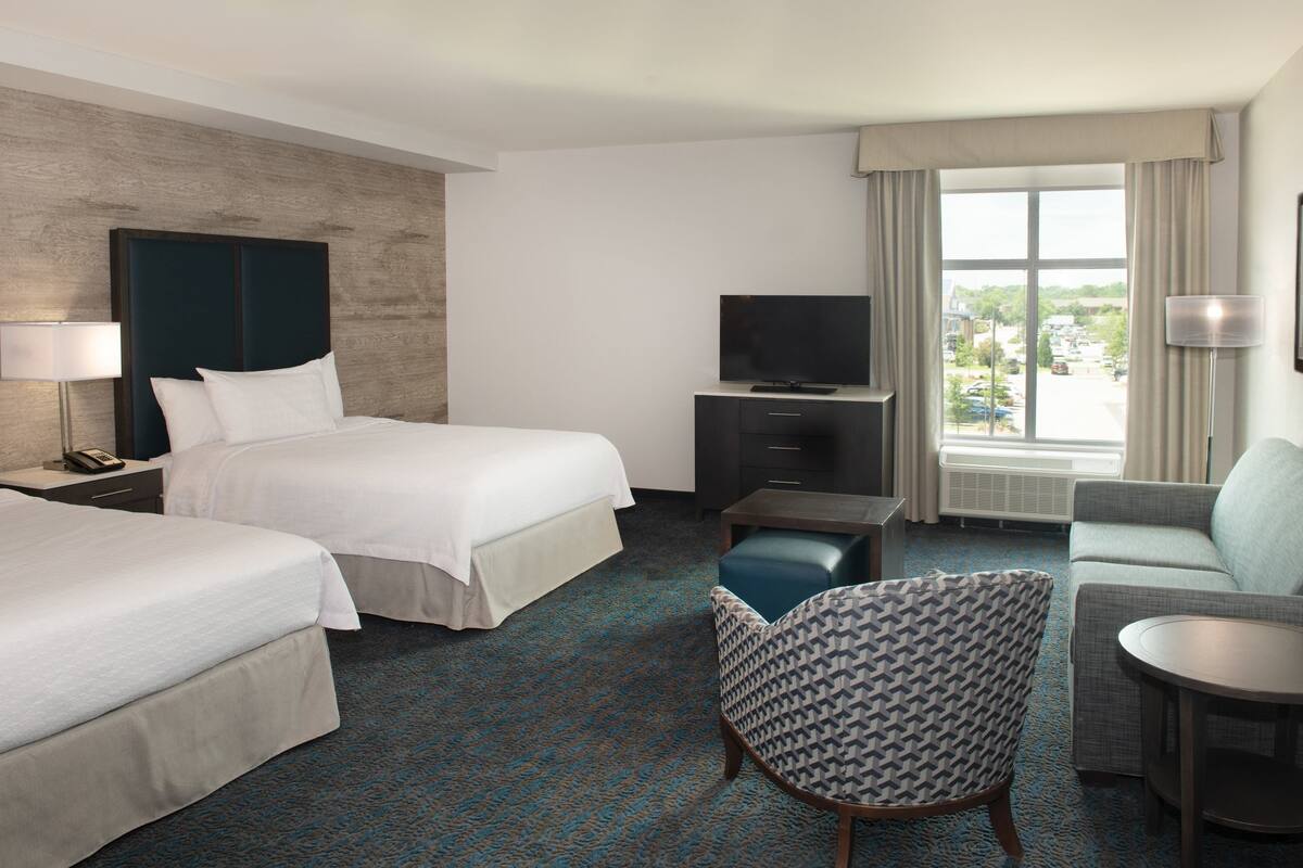 Een hotelkamer met twee bedden, een bank, een stoel, een televisie en een bureau.