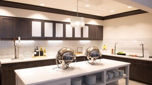 Une cuisine moderne avec des meubles en bois foncé, un plan de travail blanc et deux grands appareils pour maintenir les plats au chaud.