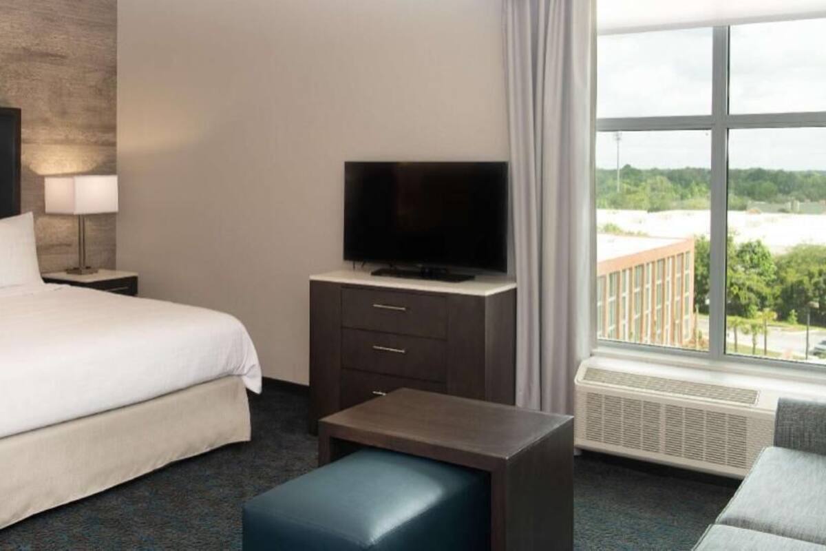 Hotelkamer met een groot bed, een televisie op een dressoir, een bureau, een stoel en uitzicht op een gebouw.