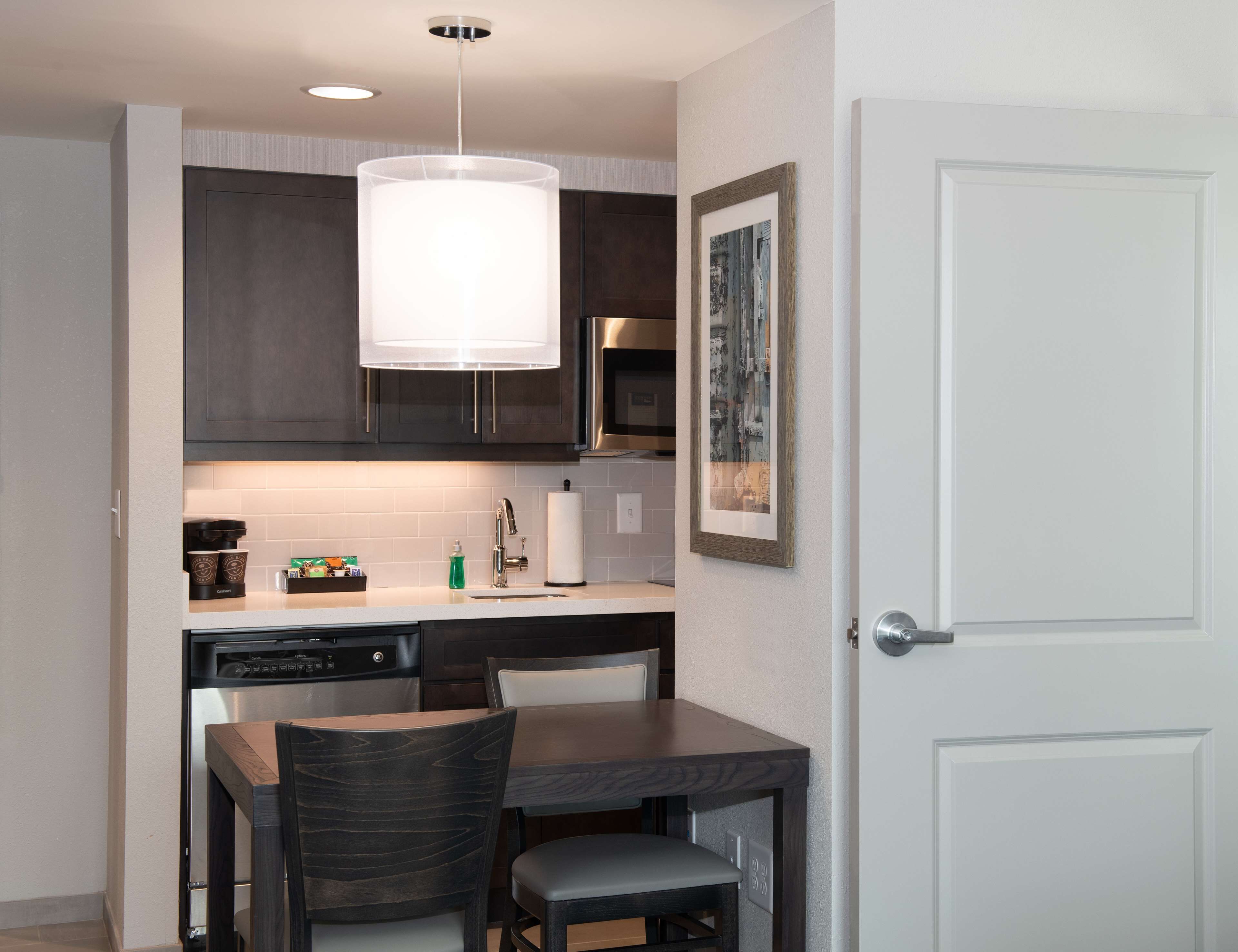 A compact kitchen with dark cabinetry, a white countertop, a built-in dishwasher, and a pendant light.
