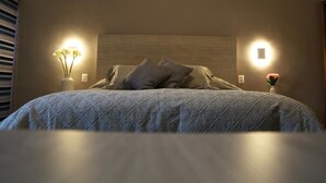 A neatly made bed with a patterned bedspread, two bedside lamps, and a vase with flowers on the nightstand. - Casa Massima Hotel (León)