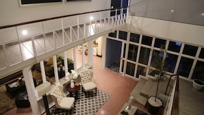 A spacious indoor area with a high ceiling, a balcony with a railing, and a seating area with chairs and a table. - Casa Massima Hotel (León)