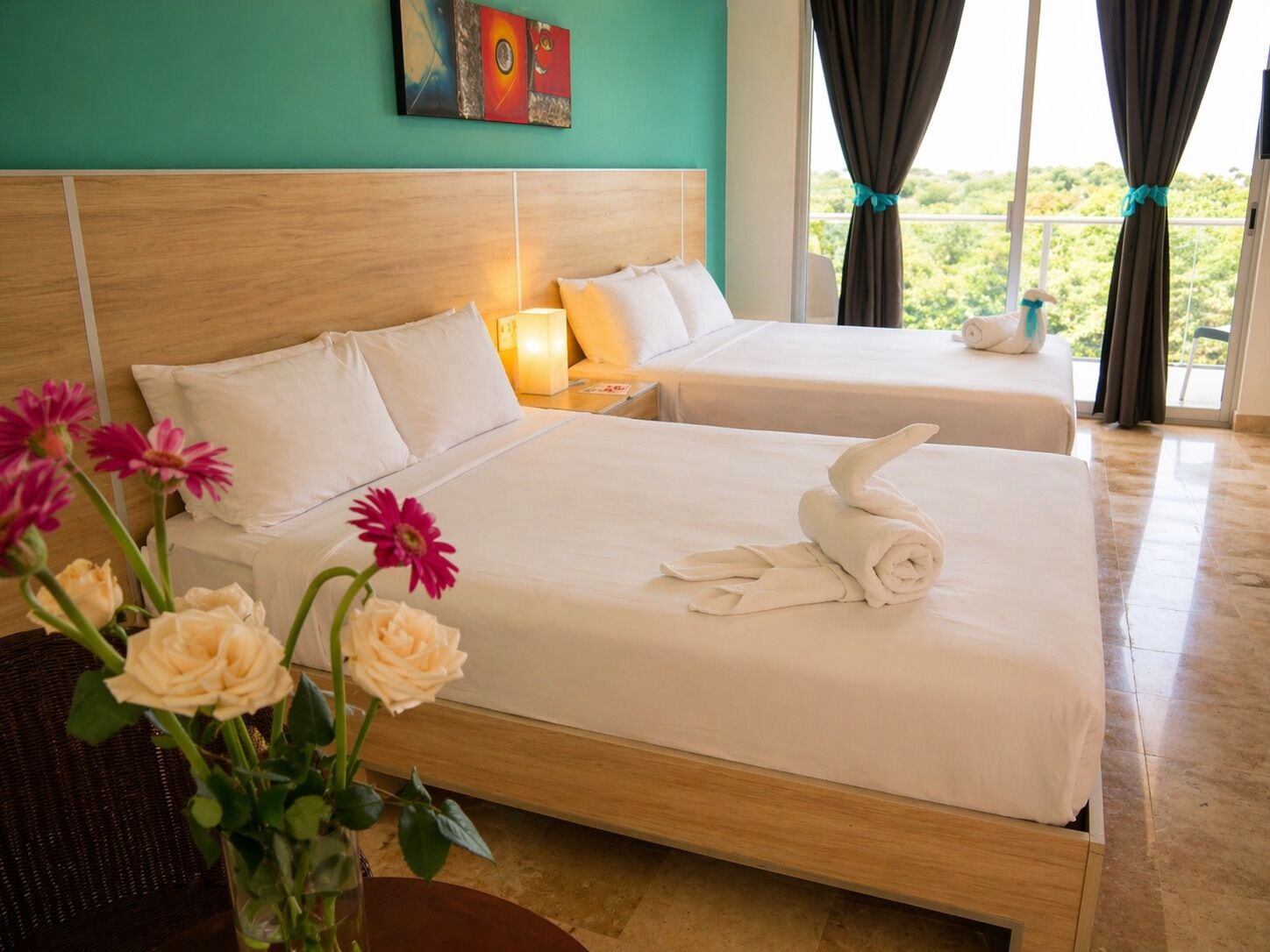 Habitación de hotel con dos camas, cabecero de madera, un cuadro en la pared y vistas al exterior con vegetación.