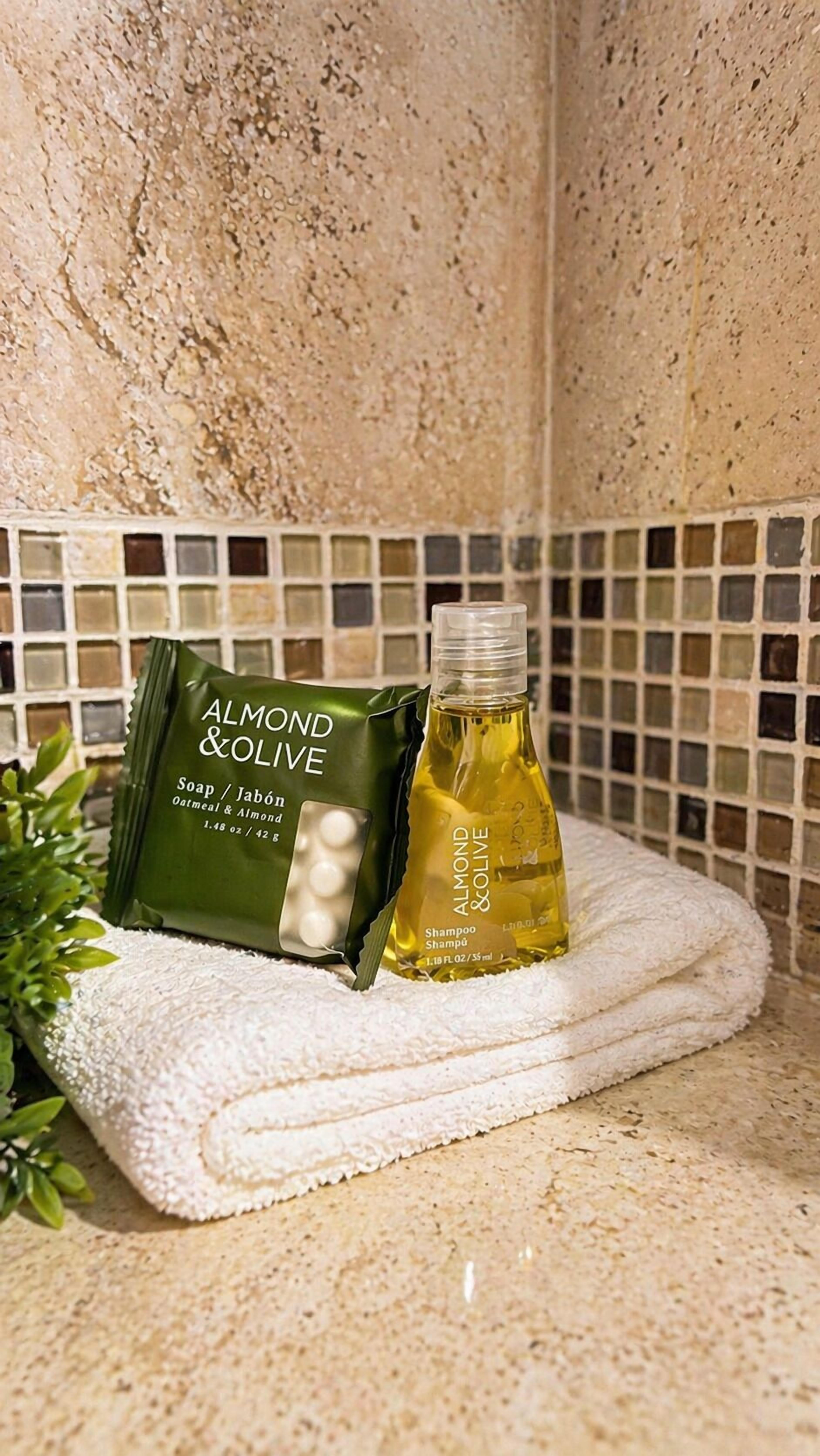 Un baño con pared de azulejos, una barra de jabón verde y una botella de champú sobre una toalla.