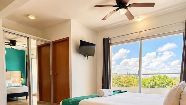 A hotel room with a bed, a ceiling fan, a TV, and a large window with a view. - PUNTA ESMERALDA Hotel Boutique (Playa del Carmen)