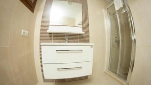 A bathroom with a shower, a mirror, and a cabinet with drawers.