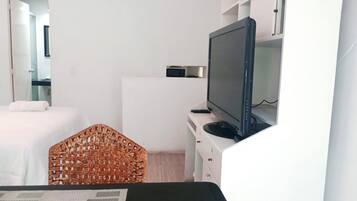 Habitación de hotel con cama, televisor sobre un mueble bajo, una mesita pequeña y una silla de mimbre.