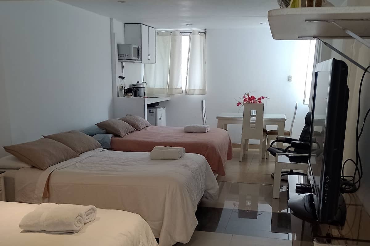 A hotel room with two beds, a desk with a computer, a TV, and a small kitchenette.