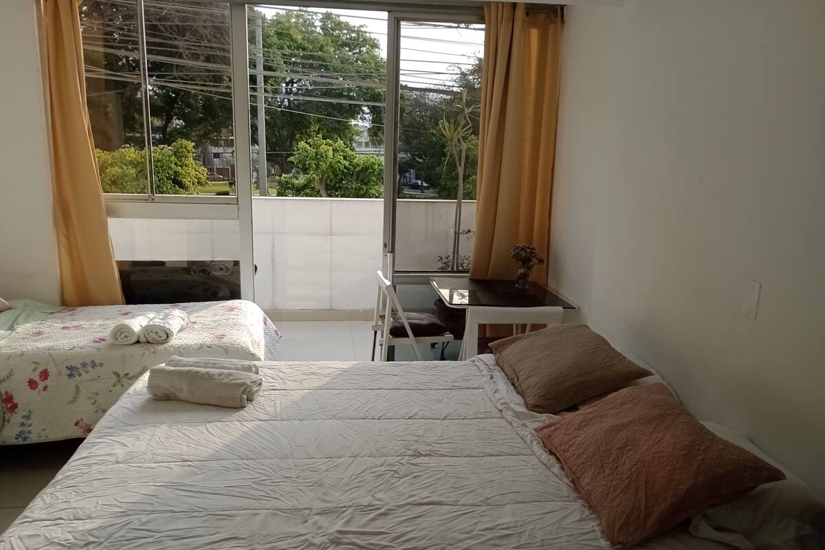 A hotel room with two beds, a small table, and a view of the outdoors.