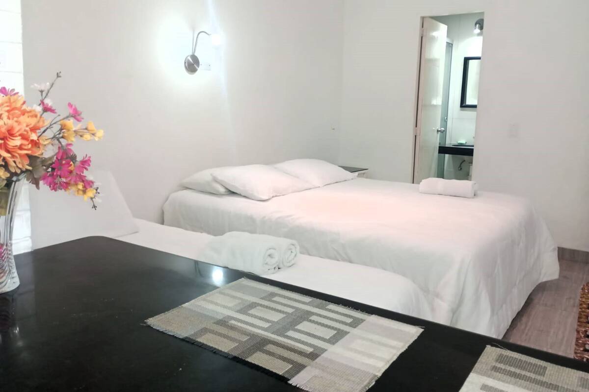 A hotel room with a bed, a bedside table with a towel, a vase with flowers, and a mirror.