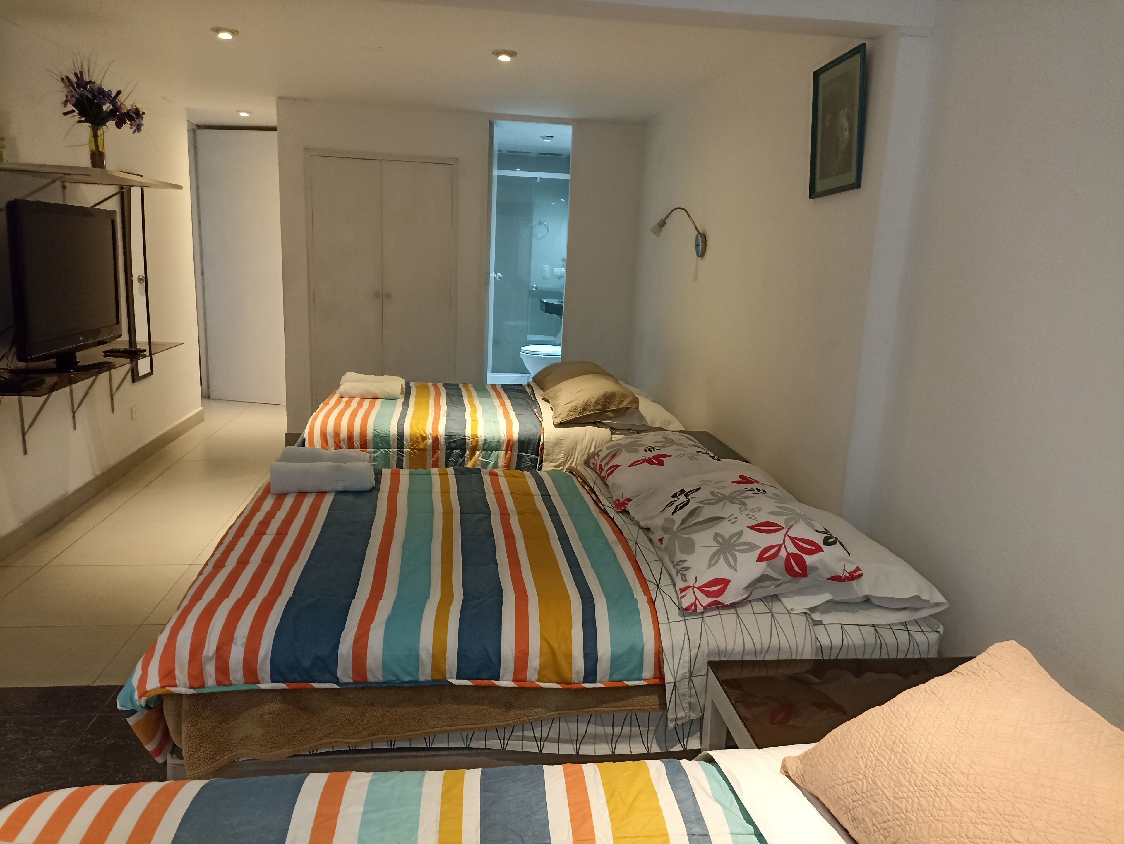 Un dormitorio con cama, televisor y baño visible a través de una puerta abierta.