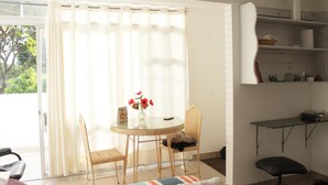 A room with a glass table, wicker chairs, a sofa, and a small desk with shelves.