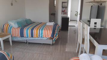 Un dormitorio con cama, escritorio y silla. Se ve un baño al fondo.