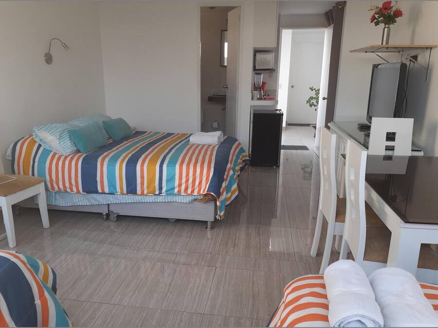 Un dormitorio con cama, escritorio y silla. Se ve un baño al fondo.