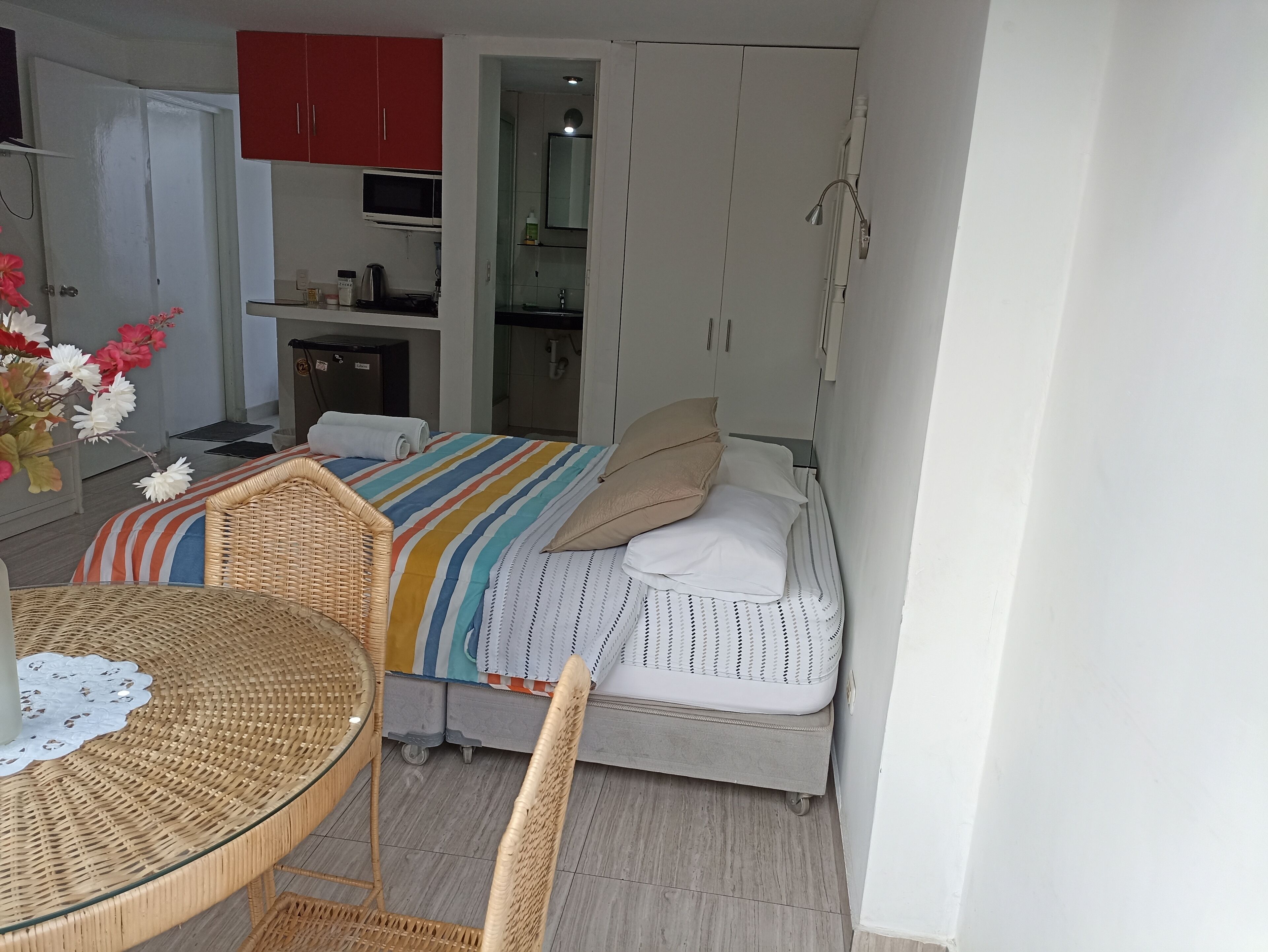 Un dormitorio compacto con cama, una kitchenette pequeña, una zona de comedor con mesa y sillas y un baño con ducha.