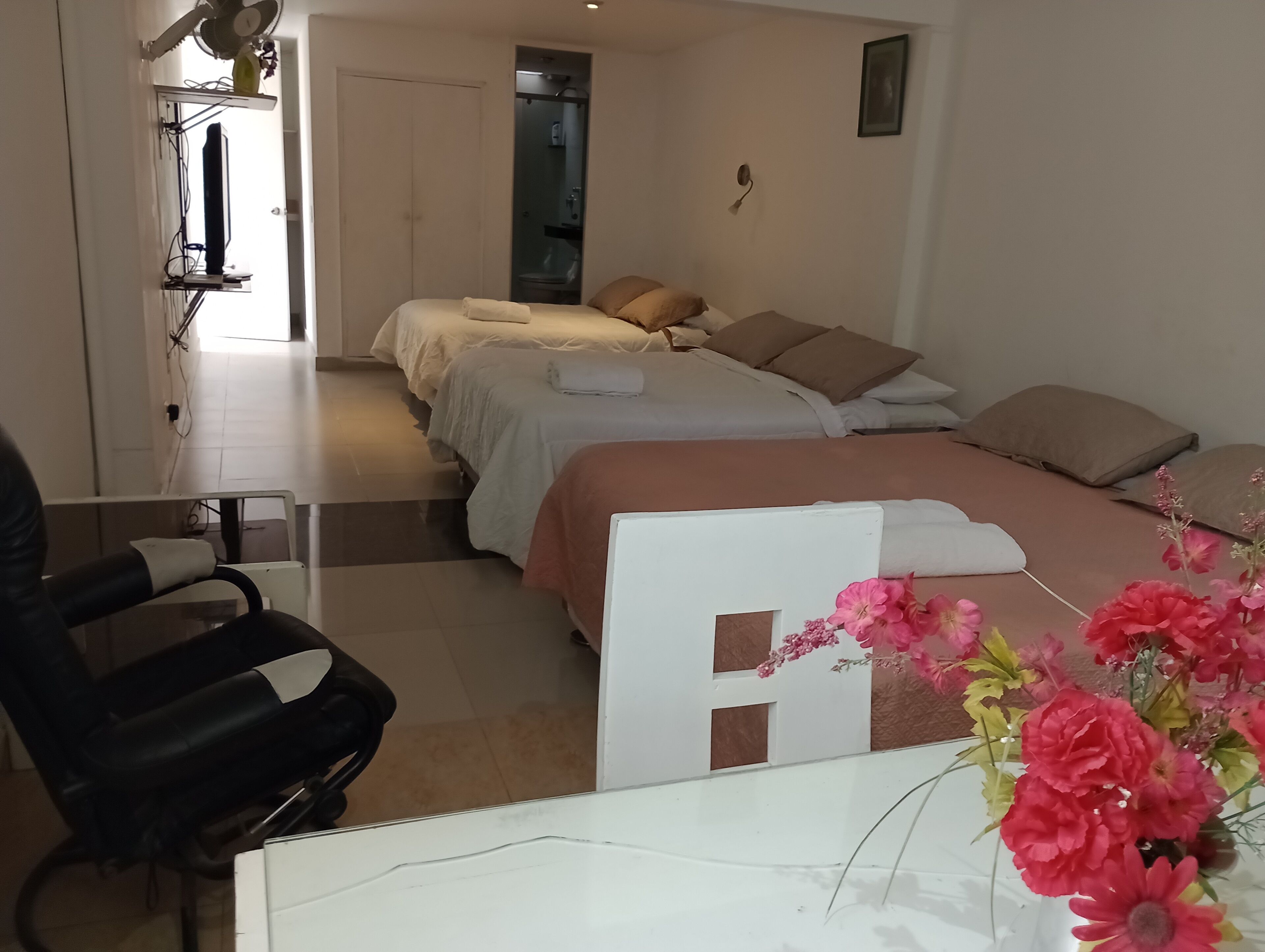 Habitación de hotel con dos camas, un escritorio, una silla y un baño visible a través de una puerta abierta.