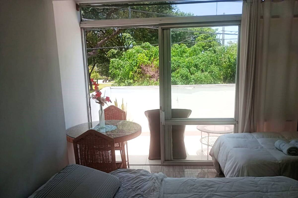 A bedroom with a bed, a small table with a vase of flowers, and a view of a garden through a sliding glass door.