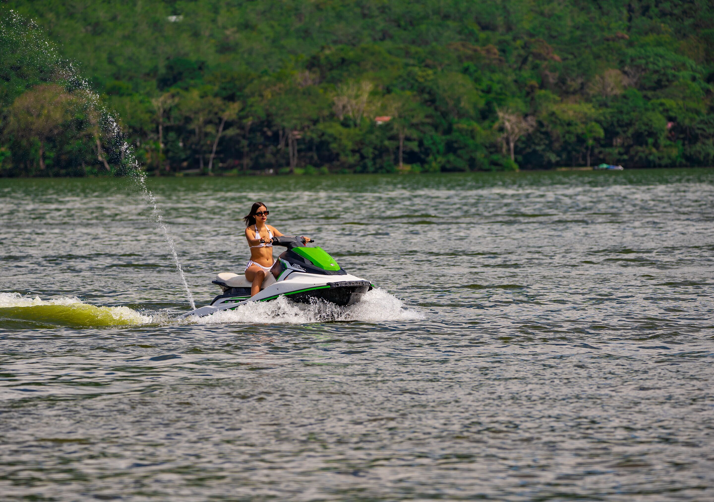 Una persona practicando esquí acuático en un lago con una orilla boscosa al fondo.