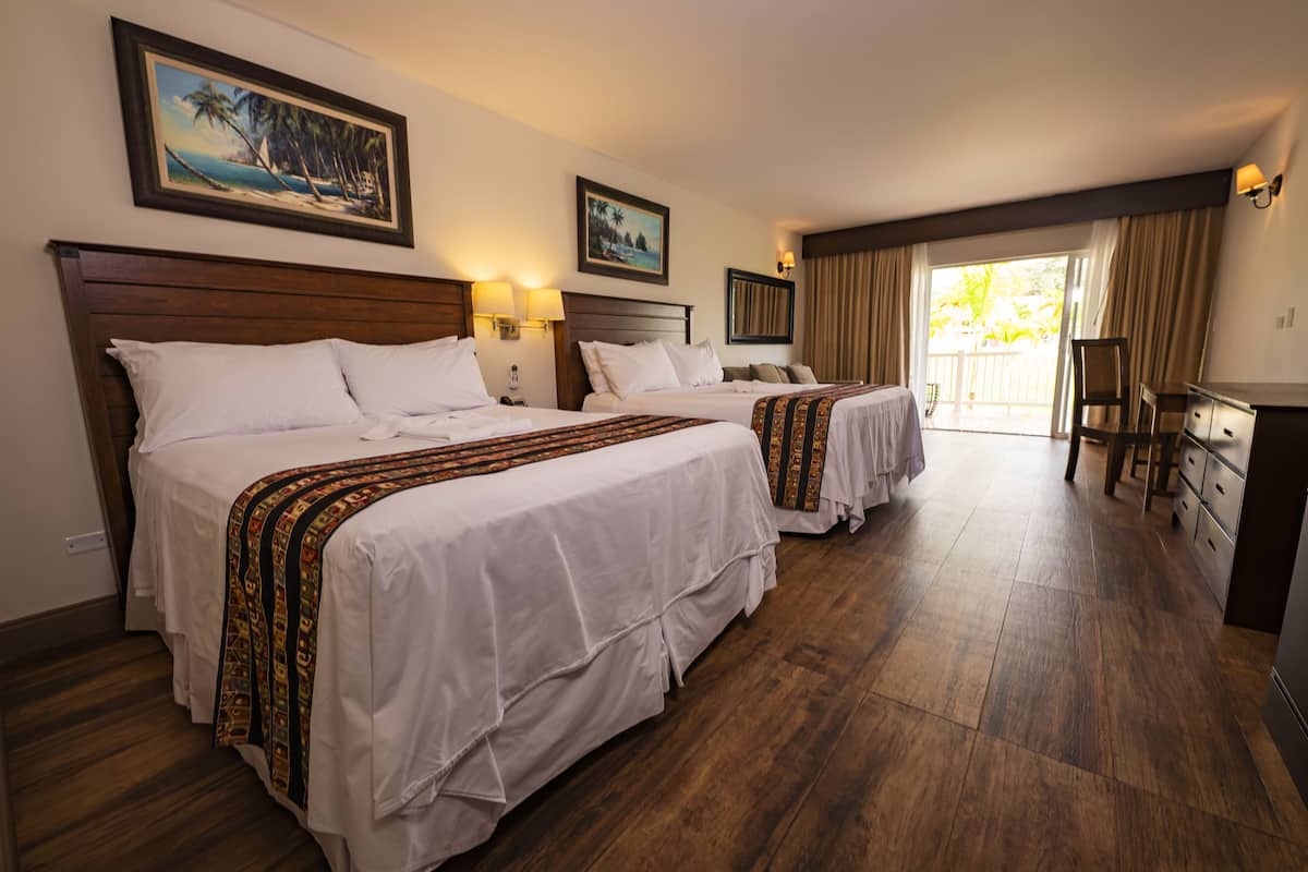 A hotel room with two beds, wooden flooring, and a balcony with curtains.