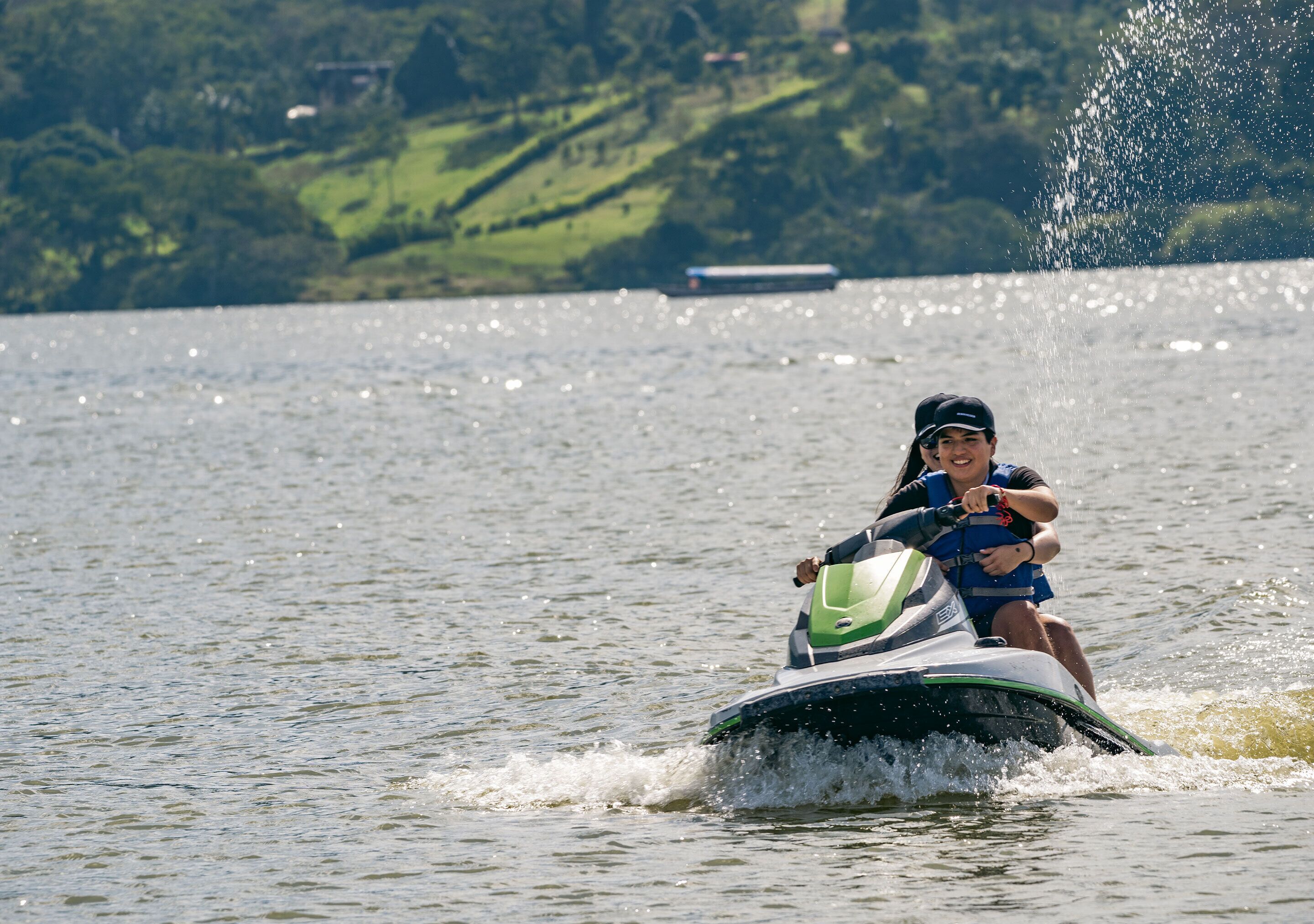 A person jet-skiing on a lake with a boat in the background.