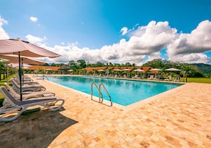 A swimming pool with lounge chairs and umbrellas, surrounded by a brick patio and greenery.