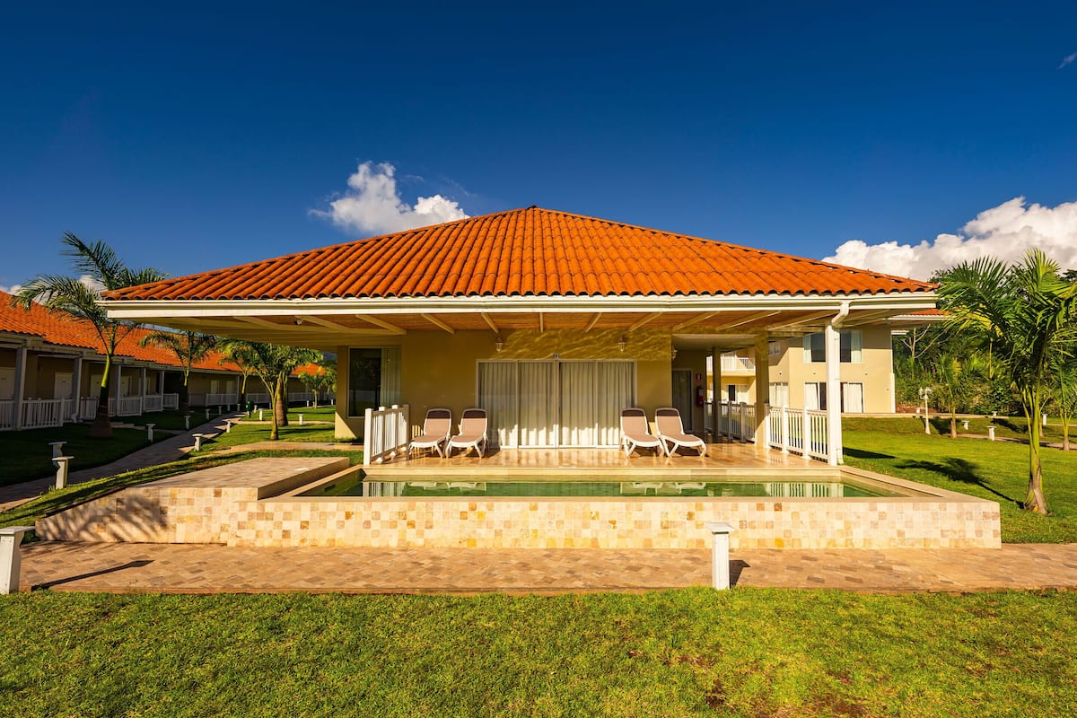 A resort with a swimming pool, covered patio, and multiple lounge chairs.