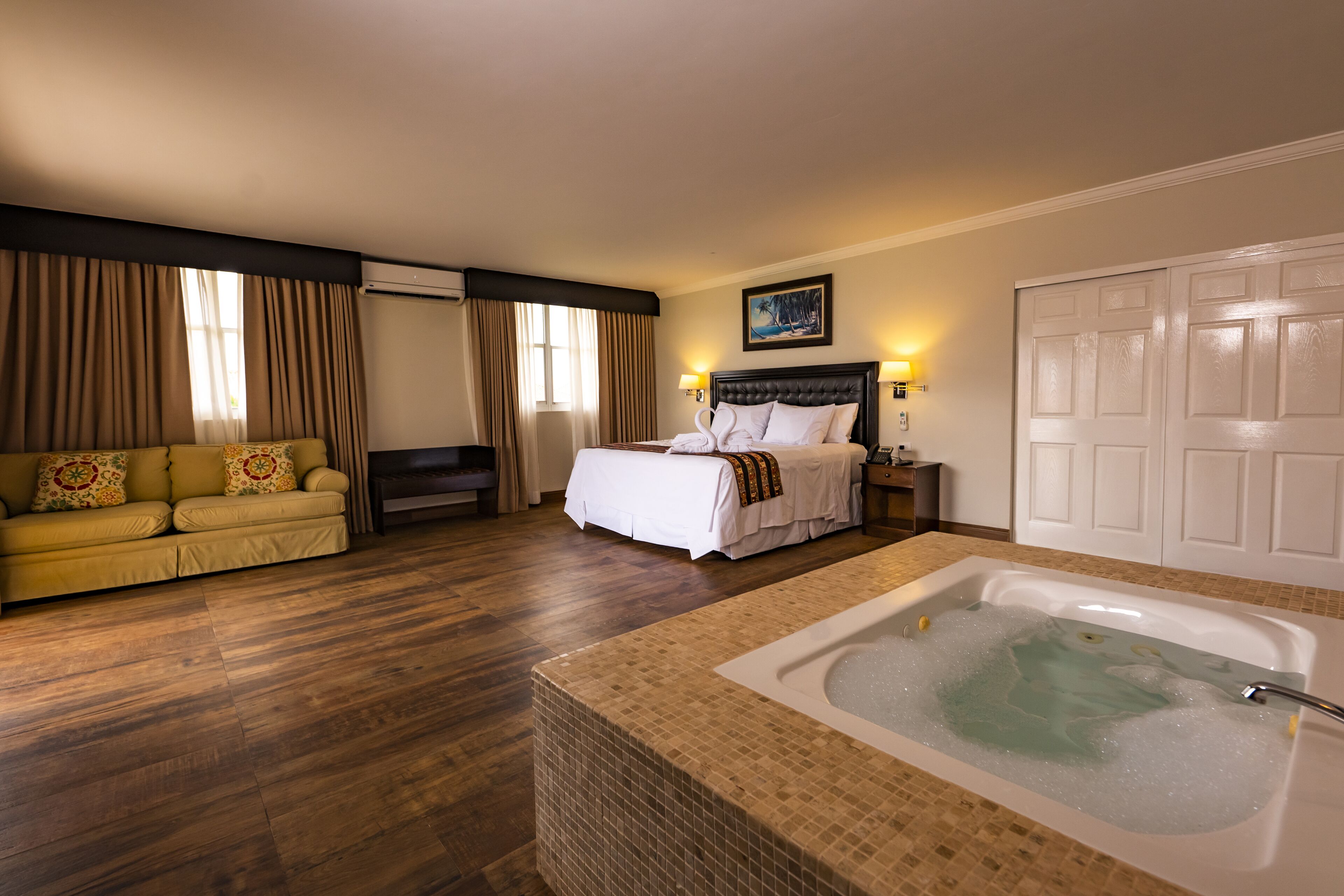 Una habitación de hotel con una cama grande, un sofá, una bañera y una puerta.
