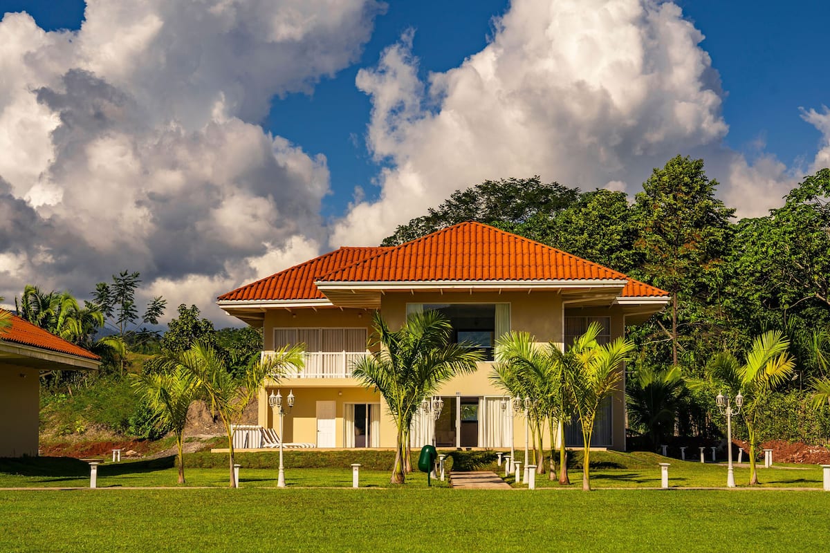 A two-story house with a red roof, surrounded by a well-maintained lawn and palm trees.