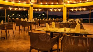 An outdoor dining area with tables and chairs, string lights, and a view of the mountains at dusk. - Bella Terra Laguna Azul Resort & Spa (Sauce)