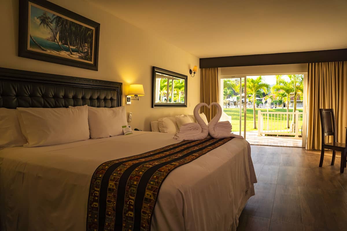 A hotel room with a large bed, a view of the outdoors, and a balcony with a chair.
