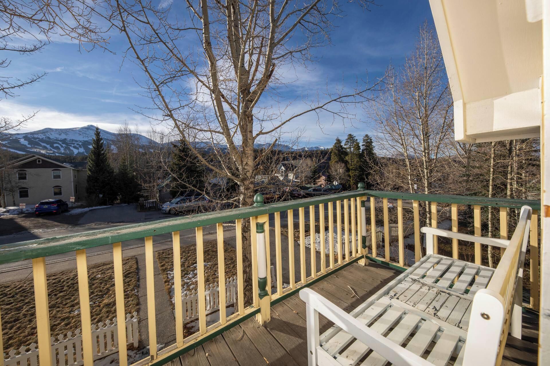 A wooden deck with a white chair, a green railing, and a view of a mountain and houses in the background.