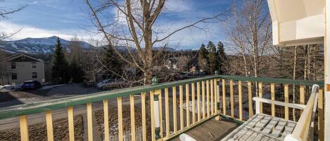 A wooden deck with a white chair, a green railing, and a view of a mountain and houses in the background.