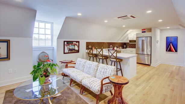 A modern kitchen with a refrigerator, a dining area with a sofa and chairs, and a large window providing natural light. - Enviable Location Blending Charm and Comfort (Charleston)