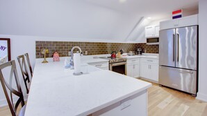 A modern kitchen with white cabinets, a stainless steel refrigerator, and a brick backsplash. - Enviable Location Blending Charm and Comfort (Charleston)