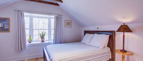 A bedroom with a bed, a window with curtains, a bedside table with a lamp, and a small potted plant.