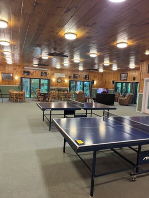 A room with wooden walls, ceiling fans, and a ping pong table.