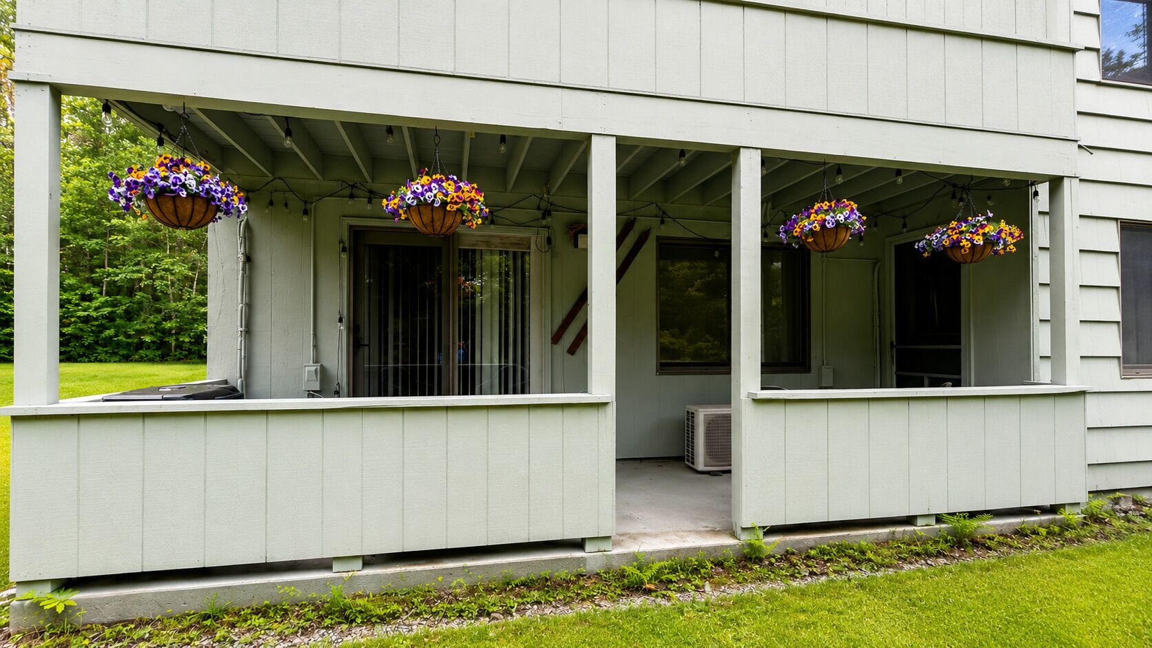 Une maison dotée d’un porche couvert, de jardinières suspendues et d’un appareil de climatisation visible.