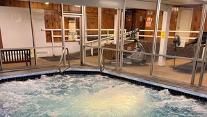 Ein Whirlpool mit umlaufender Holzterrasse, einer Glasscheibe und einer Holzwand mit Fenster.