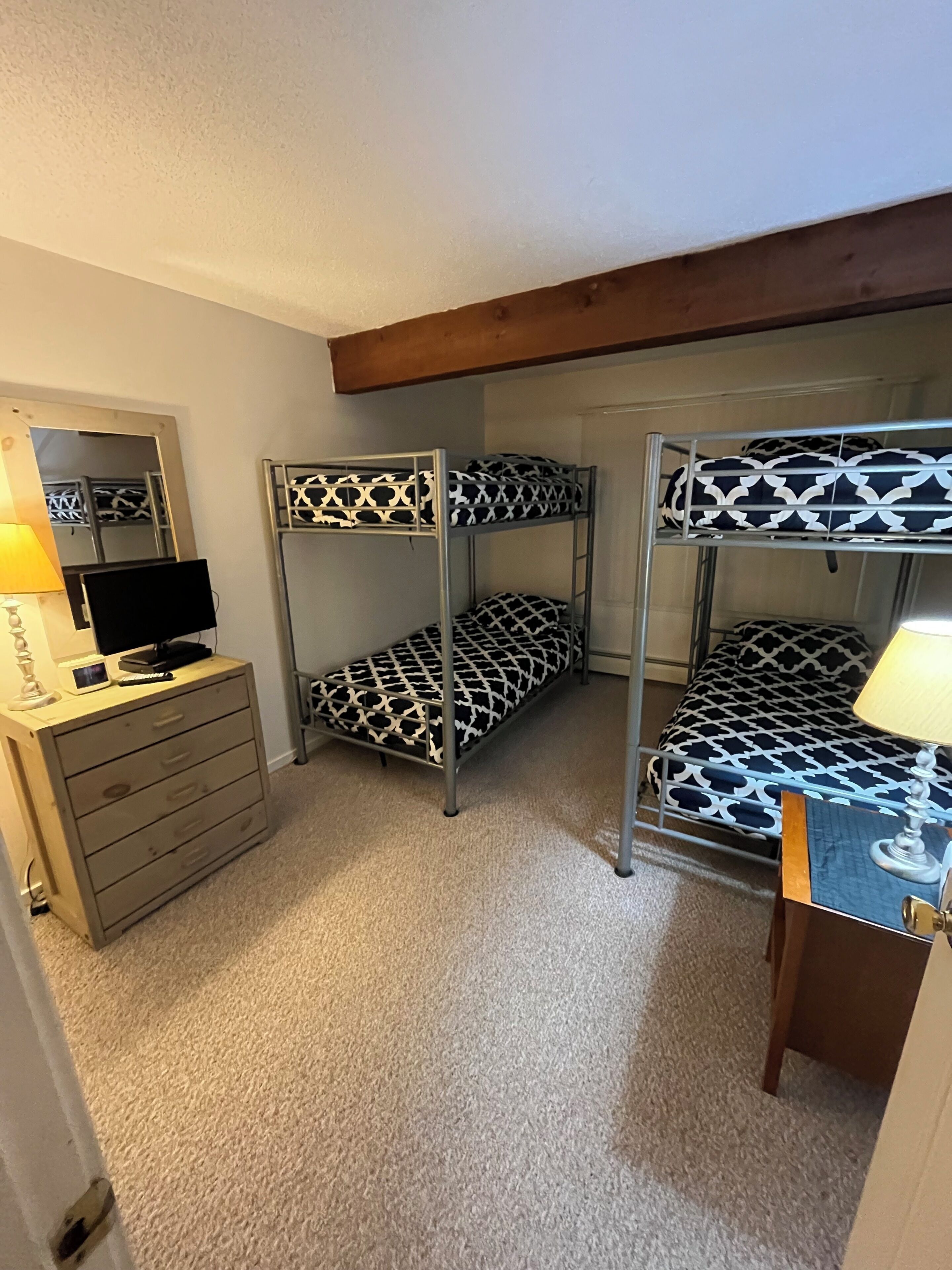 Quarto com beliches, cômoda, televisão e luminária.