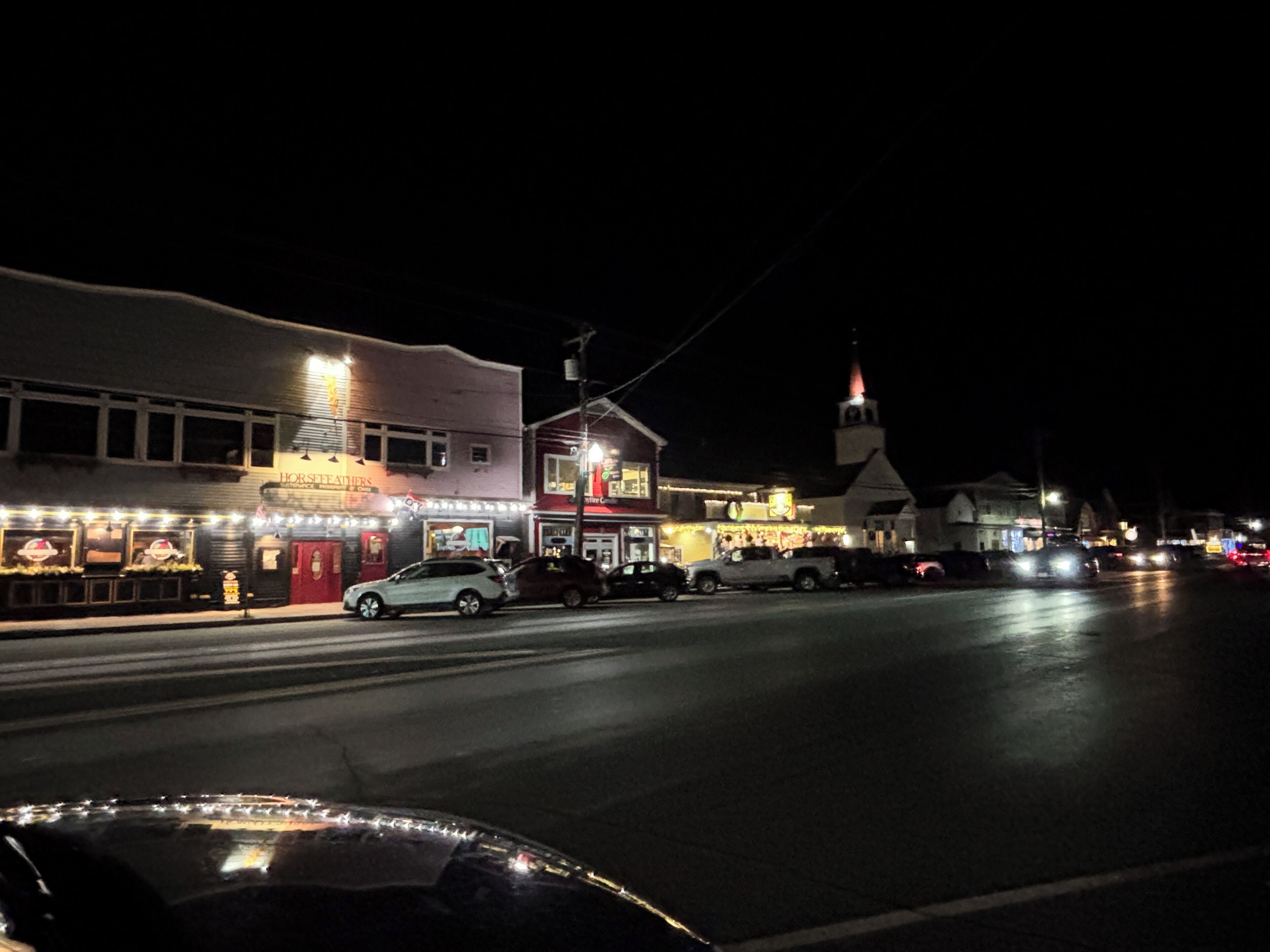 A street view at night with illuminated storefronts, including a restaurant and a church.