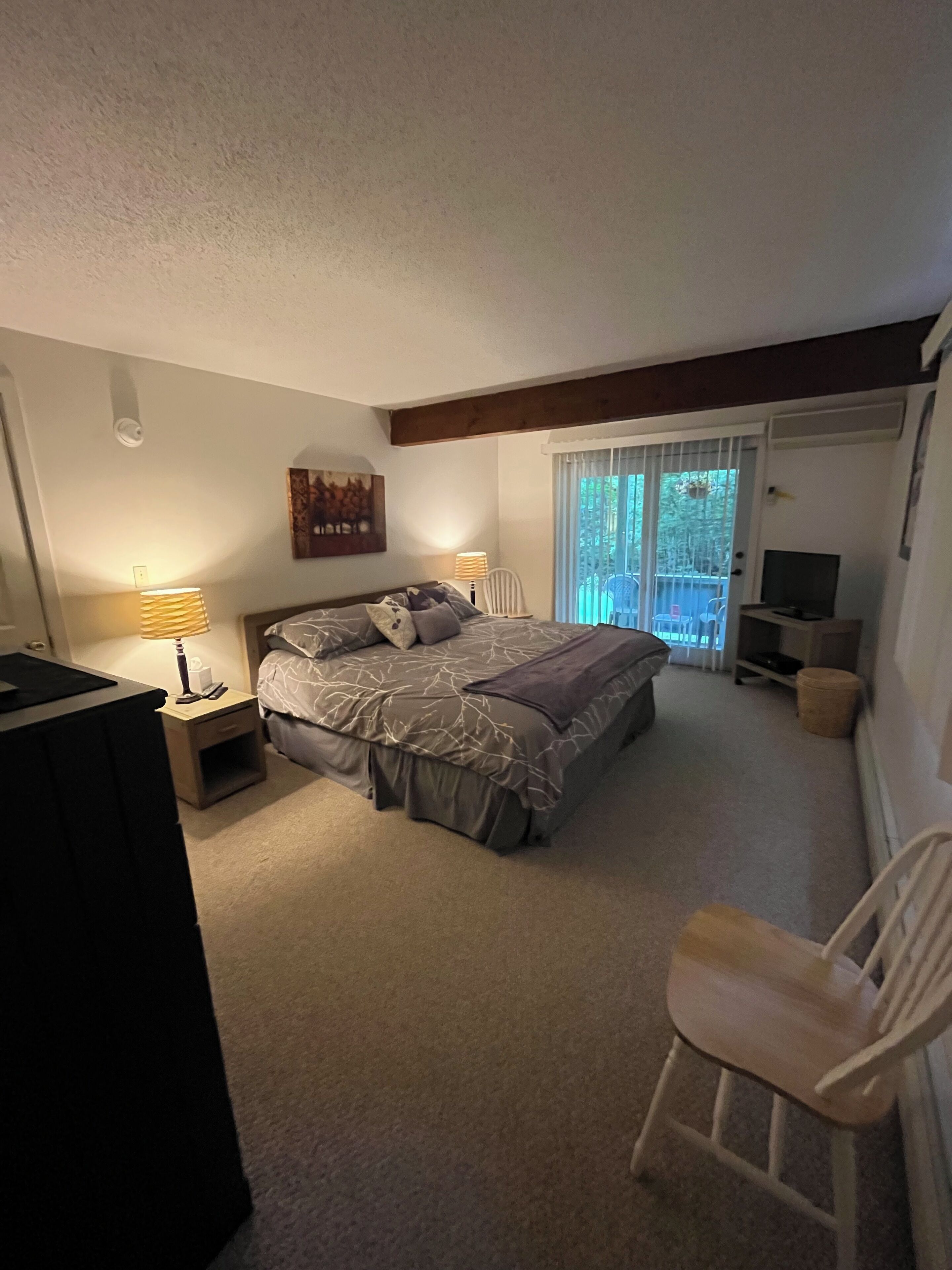 A bedroom with a bed, a chair, a TV, and a window with blinds.